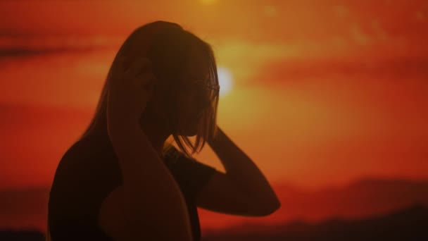 一个女人在大耳机上欣赏音乐的轮廓 被夕阳西下的温暖光芒所捕捉 宁静的景象唤起了一种宁静的感觉和单纯的音乐享受 — 图库视频影像