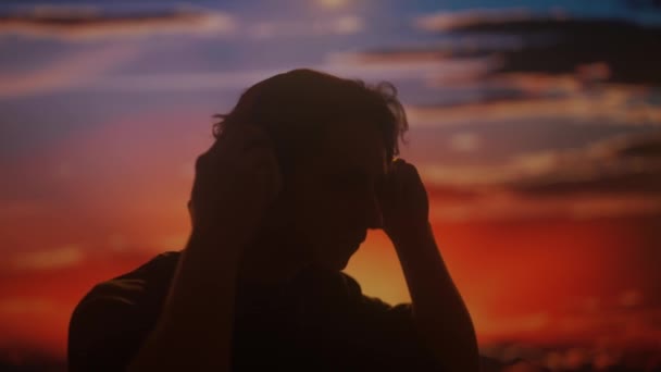Büyük Kulaklıklarla Müziğin Keyfini Çıkaran Bir Adamın Silueti Batan Güneşin — Stok video