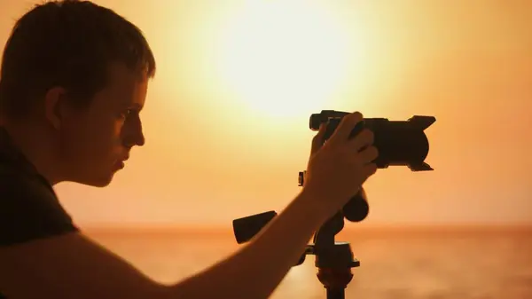 This image showcases the silhouette of a male photographer engrossed in taking photos during the golden hour. The warm sunset in the background highlights the peaceful moment of creativity.