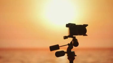 Üç ayaklı bir kameranın çarpıcı silueti canlı bir günbatımının arka planına karşı film çekmenin özünü yakalar. Anları yakalama sanatı.