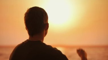 Gün batımında arka planda bir adamın silueti Koreli bir kalbi parmaklarıyla günbatımına doğru kaldırıyor, sevgiyi ve doğayla bağlantıyı simgeliyor..