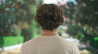 Geniş kablosuz kulaklıkla müzik dinleyen genç bir adam. Bulanık bir park manzarasının önündeki yeşil ağaçlı erkek dinlenme atmosferini taşıyor. Arka plan.