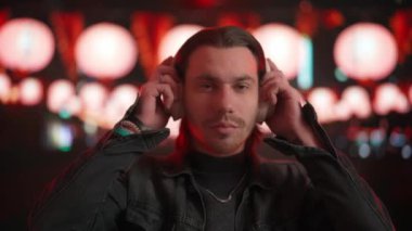 Geniş kablosuz kulaklıkla müzik dinleyen genç adam gece bulanık şehir manzarasına karşı, yanıp sönen ışıklarla. Yaşam tarzı kavramı, şehrin koşuşturma ve koşuşturmasından uzak bir tatil..