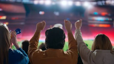 Bir spor sahasında siluet futbol fanatiklerinin heyecan verici bir fotoğrafı, kollarını havaya kaldırıp kutlama yapıyorlar, stadyumdaki aksiyondan büyüleniyorlar, o anın tutkusuna kapılıyorlar..
