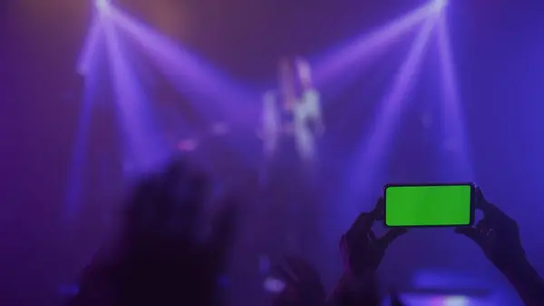 A breathtaking moment captured at a lively concert, with silhouette of hands raised up with smartphone green screen against bright stage lights, representing the shared joy.