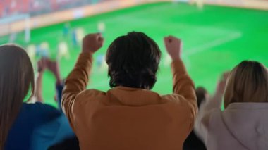 Bir spor sahasında siluet futbol fanatiklerinin heyecan verici bir fotoğrafı, kollarını havaya kaldırıp kutlama yapıyorlar, stadyumdaki aksiyondan büyüleniyorlar, o anın tutkusuna kapılıyorlar..
