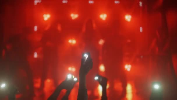 活気あふれるコンサートで捉えられた息をのむような瞬間 明るいステージライトを背景に輝く懐中電灯で手のシルエットが立ち上がり 共通の喜びを表現しました — ストック動画