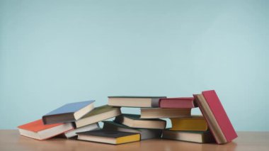 Stop motion video: renkli eski kitaplar bir yığın kaybolur ve sonra sakin mavi arka planda bir ahşap masa üzerinde kitap yığını oluşturarak tekrar ortaya çıkar.