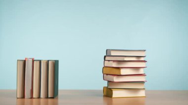 Stop Motion video: renkli kapaklı bir yığın eski kitap sakin mavi arka plana karşı ahşap bir yüzey üzerinde yeniden düzenlenir ve sonra kitaplar yığın geri döner.