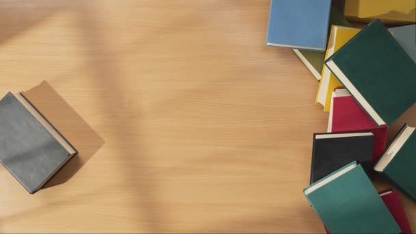 ストップモーションビデオ ページを開く木製のテーブルに移動して回転する本のトップビュー 本はカラーカバー付きの本の積み重ねに近づいています — ストック動画