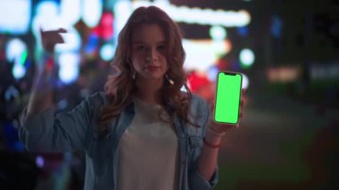 Gadget 'lar ve modern günlük hayat reklamları konsepti. Her gün akıllı telefon kullanan bir kadın. Şehirde geceleri genç bir kadın akıllı telefon kroma yeşil ekrana işaret ediyor..