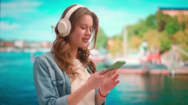 Gadget 'lar ve modern günlük hayat reklamları konsepti. Her gün akıllı telefon kullanan bir kadın. Tatilde olan genç bir kadın kulaklık takıyor, akıllı telefondan müzik dinliyor..