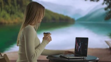 Serbest ve serbest meslek hayatı konsepti. Uzaktan çalışan ve seyahat eden bir kadın. Dağ Gölü yakınlarında çalışan, dizüstü bilgisayarda yazan, bardaktan kahve içen genç bir kadın..