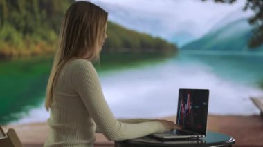 Serbest ve serbest meslek hayatı konsepti. Uzaktan çalışan ve seyahat eden bir kadın. Dağ Gölü yakınlarında çalışan genç bir kadın, dizüstü bilgisayarda yazıyor, proje üzerinde çalışıyor..