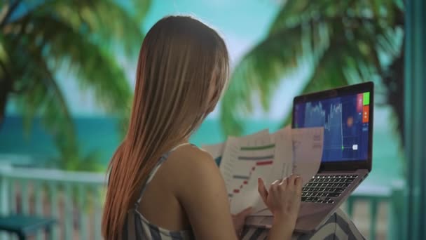 フリーランスと自営業ライフスタイルのコンセプト 遠くから働き 旅をする女性 若い女性フリーランサーは 熱帯のビーチリゾートでラップトップで作業する紙文書を保持しています 背中のショット — ストック動画