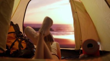 Kamp ve macera konsepti. Kamp alanında gezen, yürüyüş yapan, doğayı keşfeden biri. Genç bir kadın gün batımında çadırın içinde uzanmış plaja bakıyor, dışarıda tatil ve tatil yapıyor..
