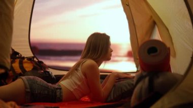 Kamp ve macera konsepti. Kamp alanında gezen, yürüyüş yapan, doğayı keşfeden biri. Genç bir kadın gün batımında çadırın içinde dizüstü bilgisayarda, tatilde ve dışarıda çalışıyor..