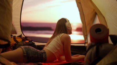 Kamp ve macera konsepti. Kamp alanında gezen, yürüyüş yapan, doğayı keşfeden biri. Genç bir kadın, gün batımında sahilde çadırın içinde kulaklıkla müzik dinliyor..