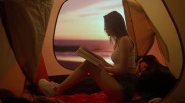 Kamp ve macera konsepti. Kamp alanında gezen, yürüyüş yapan, doğayı keşfeden biri. Gün batımında sahilde çadırın içinde kitap okuyan genç bir kadın. Tatil ve açık havada tatil..