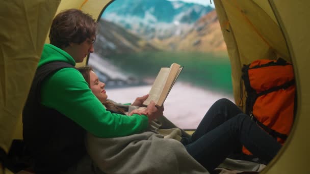 キャンプと冒険のコンセプト キャンプ場の人々は 自然を探索し 旅行し ハイキングします 若い愛するカップルは 山の湖岸のテントの中の本を読みます 休日やアウトドアでの休暇 — ストック動画