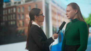Canlı TV haber yayın konsepti. Bayan sunucu dışarıda canlı yayında. Kadın sunucu gazeteci sokakta genç bir bayanla röportaj yapıyor, arka planda şehir geçmişi var..
