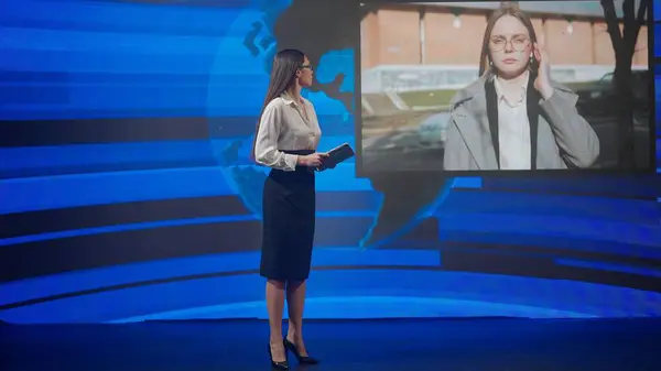 Live tv news broadcasting concept. Female presenter in the studio. Woman news host presenting daily events, talking on air with reporter outside, breaking news background at the back.