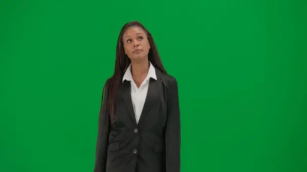 Tv news report and live broadcasting advertisement concept. Female reporter isolated on chroma key green screen background. African American woman news host presenter in suit looking around.
