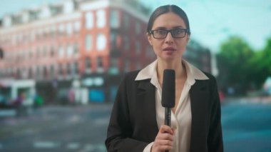 Canlı TV haber yayın konsepti. Bayan sunucu dışarıda canlı yayında. Kadın sunucu gazeteci stüdyoyla konuşuyor, kulaklık takıyor, sokakta duruyor, arka planda şehir geçmişi var..