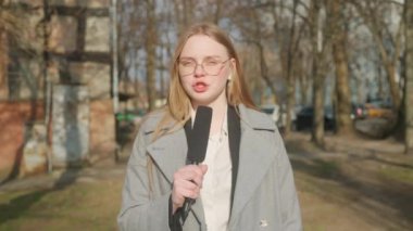 Canlı TV haber yayın konsepti. Bayan sunucu dışarıda canlı yayında. Kadın sunucu gazeteci stüdyoyla konuşuyor, kulaklık takıyor, sokakta duruyor, arka planda şehir geçmişi var..