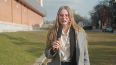 Canlı TV haber yayın konsepti. Bayan sunucu dışarıda canlı yayında. Kadın sunucu gazeteci stüdyoyla konuşuyor, kulaklık takıyor, sokakta duruyor, arka planda şehir geçmişi var..