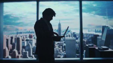 Şirket reklam konsepti. Ofiste başarılı bir iş adamı. Man ceo hedge fon üst yöneticisi dizüstü bilgisayarlı daktilo tutuyor pencere önünde çalışıyor şehir manzaralı.