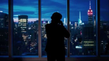 Şirket reklam konsepti. Ofiste başarılı bir iş adamı. Man ceo hedge fon üst yöneticisi pencere önünde akşam şehir manzaralı dışarı bakarak akıllı telefon konuşuyor.