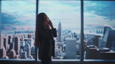 Şirket reklam konsepti. Ofiste başarılı bir iş kadını. Kadın yatırım fonu üst düzey yöneticisi sabah manzaralı pencerenin önünde akıllı telefonla konuşuyor..