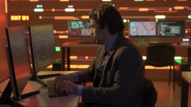 Proje yöneticisi bilgisayar bilimi konsepti. Kontrol odasında teknik destek. İnsan bilişim uzmanı ofiste kulaklık üzerinde çalışıyor. Büyük dijital ekranda altyapı verileri görünüyor..