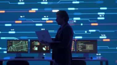 Proje yöneticisi bilgisayar bilimi konsepti. Güvenlik ofisinde dizüstü bilgisayarı olan bir adamın silueti, büyük dijital ekran altyapısı bilgi ağı verilerini izliyor..
