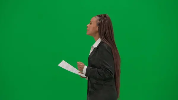 Tv news report and live broadcasting advertisement concept. Female reporter isolated on chroma key green screen background. African American woman news host in suit reads paper documents and talks
