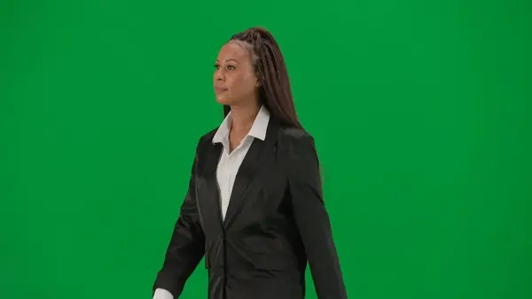 Tv news report and live broadcasting advertisement concept. Female reporter isolated on chroma key green screen background. African American woman news host presenter in suit walking looking around