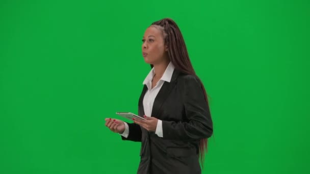 テレビニュースレポートとライブ放送広告コンセプト クロマキーの緑色の背景で隔離された女性の記者は アフリカ系アメリカ人女性のニュースホストが歩き タブレットを保持 — ストック動画