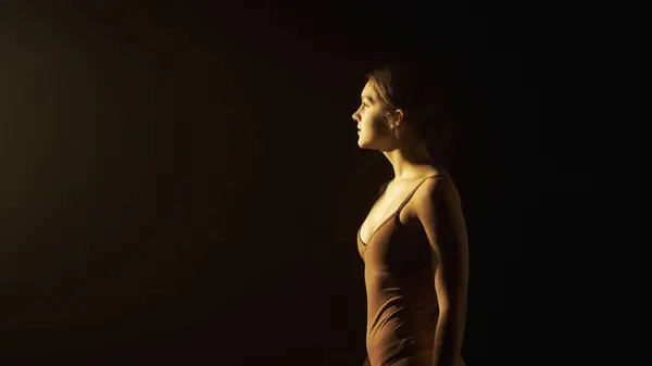 柔らかい光で暗いスタジオで少女の肖像画 女性のシルエットは柔らかい光で概説され 彼女の脆さと優雅さを強調しています サイドビュー — ストック写真