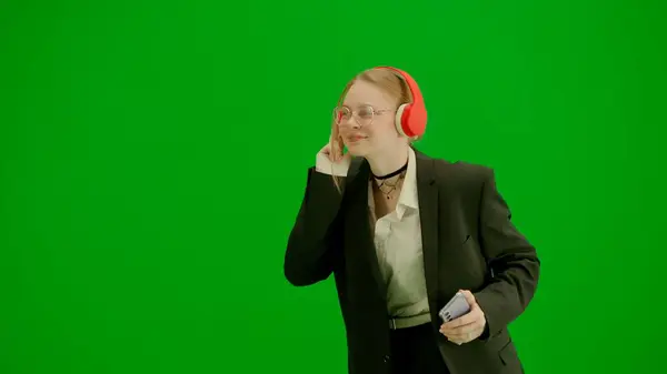 Modern businesswoman creative advertisement concept. Portrait of female in suit on chroma key green screen. Blonde business woman in formal outfit walking in headphones listening music on smartphone.