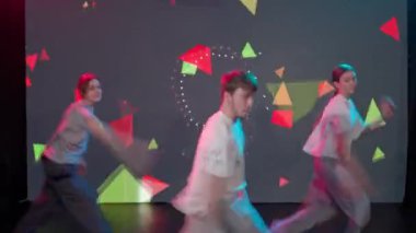 Sahne arkası video çekiminde kameraman çekim yapıyor ve yönetmen hip hop sokak tarzında dans eden dansçı üçlüsünü kontrol ediyor. İki kız ve bir adam büyük bir LED ekranda dans ediyor..