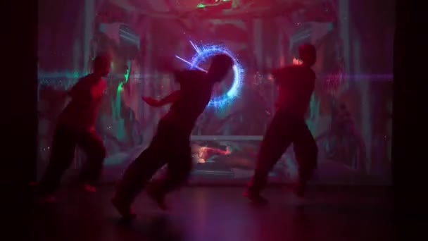 大きなLedスクリーンの輝きに浴びたモダンスタジオでは ダンサーのトリオ2人の女性と1人の男性がヒップホップのスキルを披露します 彼らの背後にあるスクリーンは 活気に満ちたダイナミックな背景を持つフリッカー — ストック動画