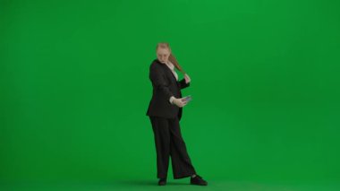 Modern iş kadını yaratıcı reklam konsepti. Krom anahtar yeşil ekranda takım elbiseli kadın portresi. Resmi kıyafetli sarışın iş kadını elinde akıllı telefonuyla selfie çekiyor..