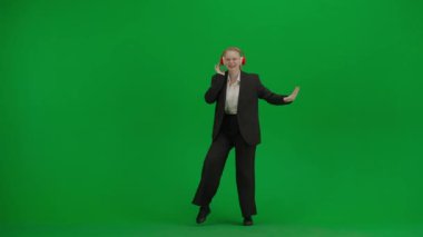 Modern iş kadını yaratıcı reklam konsepti. Krom anahtar yeşil ekranda takım elbiseli kadın portresi. Resmi kıyafetli, kulaklıklı, müzik dinleyen ve dans eden sarışın bir iş kadını..