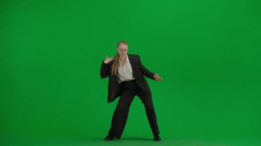 Modern iş kadını yaratıcı reklam konsepti. Krom anahtar yeşil ekranda takım elbiseli kadın portresi. Resmi kıyafetli sarışın iş kadını kameraya poz verip eski moda tekno dansı yapıyor..