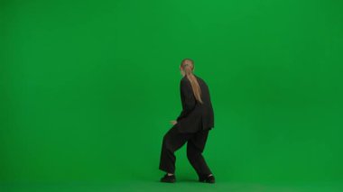 Siyah takım elbiseli kadın yeşil ekranda kromakeyle neşeyle dans ediyor. Modern iş kadını yaratıcı reklam konsepti.
