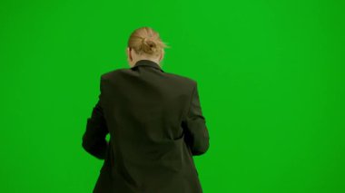 Modern iş kadını yaratıcı reklam konsepti. Krom anahtar yeşil ekranda takım elbiseli kadın portresi. Resmi kıyafetli sarışın bir iş kadını el saatini kontrol ediyor ve koşmaya başlıyor. Geri