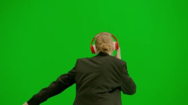 Modern iş kadını yaratıcı reklam konsepti. Krom anahtar yeşil ekranda takım elbiseli kadın portresi. Resmi kıyafetli sarışın iş kadını kulaklıkla yürüyor akıllı telefondan müzik dinliyor.