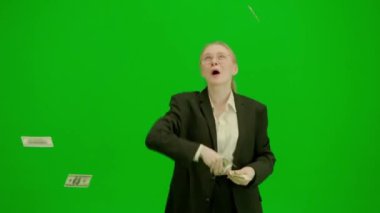 Modern iş kadını yaratıcı reklam konsepti. Krom anahtar yeşil ekranda takım elbiseli kadın portresi. Mutlu iş kadını havaya para atıp dans ediyor..
