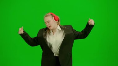 İş kadını kulaklıkla müzik dinliyor ve neşeyle dans ediyor. İş elbiseli kadın yeşil ekranda kromakey ile. Modern iş kadını yaratıcı reklam konsepti.
